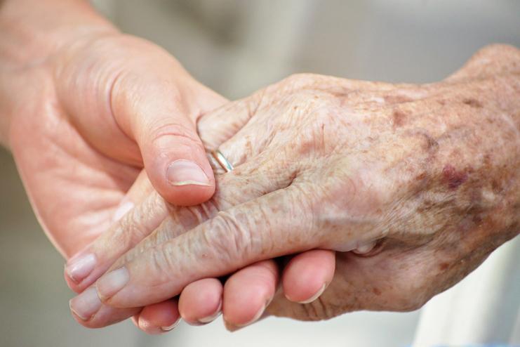 Nahaufnahme zweier Hände, eine ältere und eine jüngere, die sich liebevoll halten.