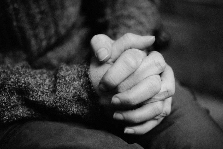 Nahaufnahme von zwei Händen, die ineinander verschränkt sind, vor einem unscharfen Hintergrund.